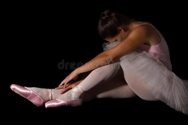 女舞者坐在地板上，神情<strong>忧伤</strong>，穿着粉红色<strong>的</strong>芭蕾舞裙
