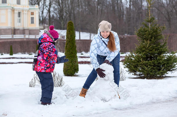 快乐妈妈带着孩子在冬季公园里用雪堆雪人