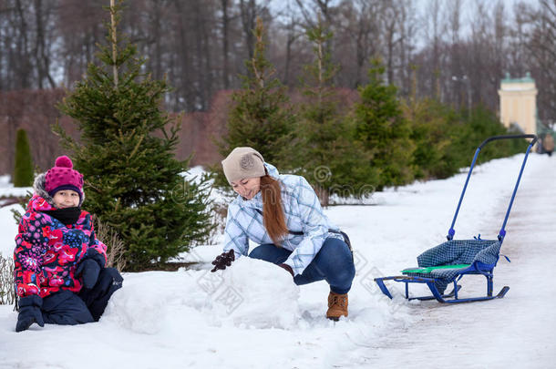 妈妈在冬天的街上帮女儿堆雪人