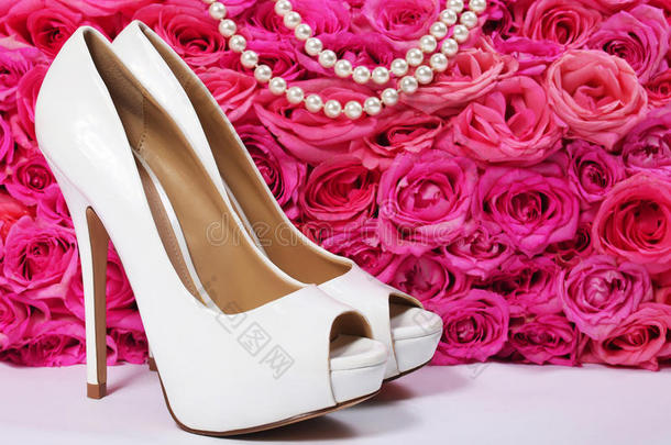 新娘鞋和玫瑰。粉色花朵上的白色高跟鞋