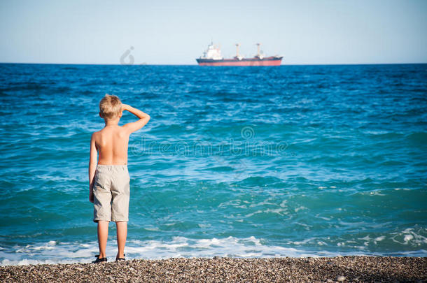 小男孩站在沙滩上看着船。