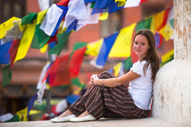 年轻女孩坐在佛塔上，背景上飘扬着经幡。旅行。