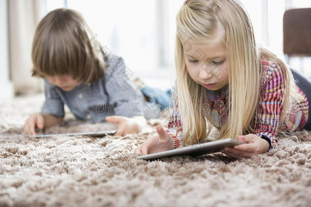 可爱的女孩和<strong>弟弟</strong>在客厅的地毯上使用数码平板电脑