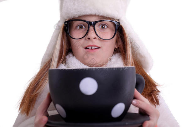 年轻漂亮的女孩戴着眼镜，戴着一顶白色的冬帽，手里拿着一个<strong>大杯子</strong>