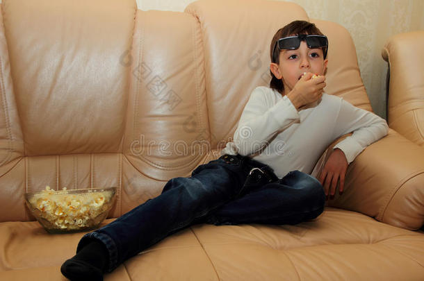 男孩拿着爆米花坐在沙发上，兴致勃勃地看电视