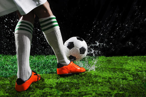 足球运动员在绿色草地上踢球，黑色背景下透明的水飞溅着