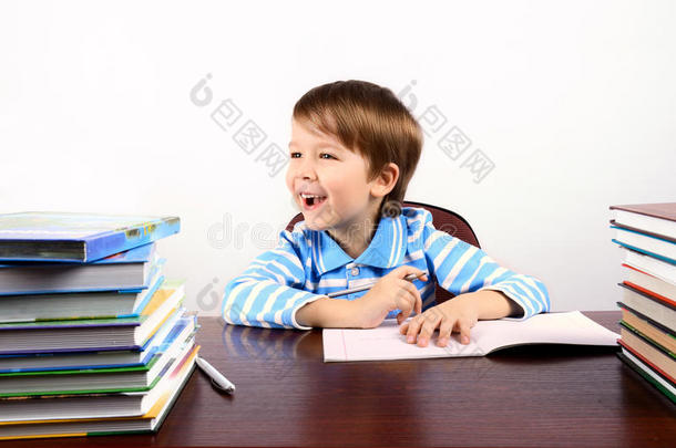 笑眯眯的男孩拿着许多书坐在书桌旁
