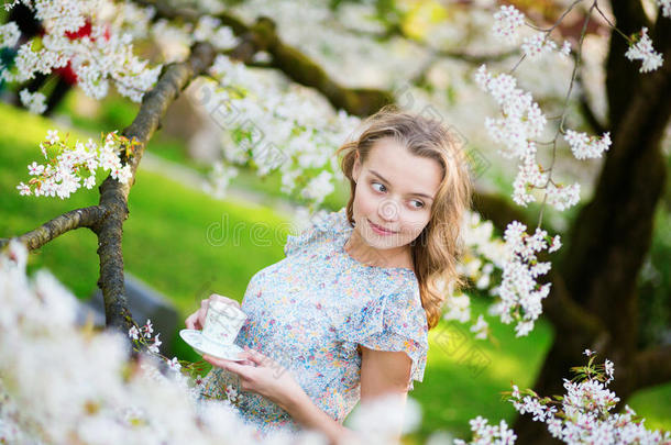 美丽的女人在樱桃园里喝着茶