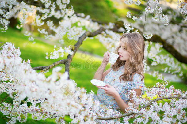 美丽的女人在樱桃园里喝着茶