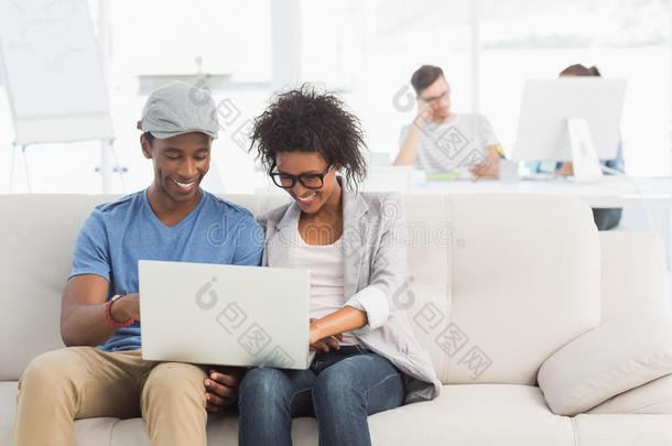 一对夫妇在创意办公室和同事一起使用笔记本电脑