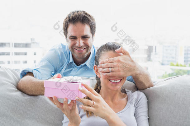 一个男人在沙发上送了一份粉红色的礼物给他的女朋友惊喜