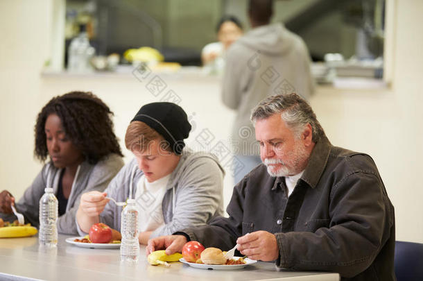 在无家可归者收容所里，人们坐在餐桌旁吃东西