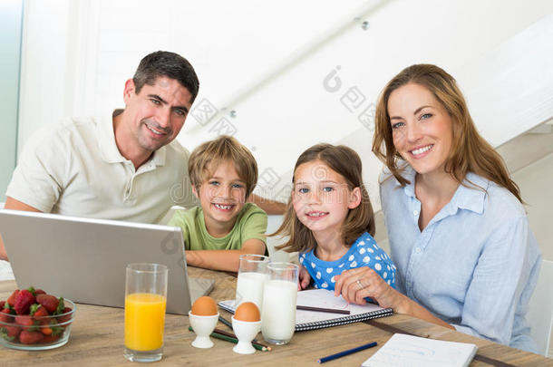 一家人在吃早餐时使用笔记本电脑的照片