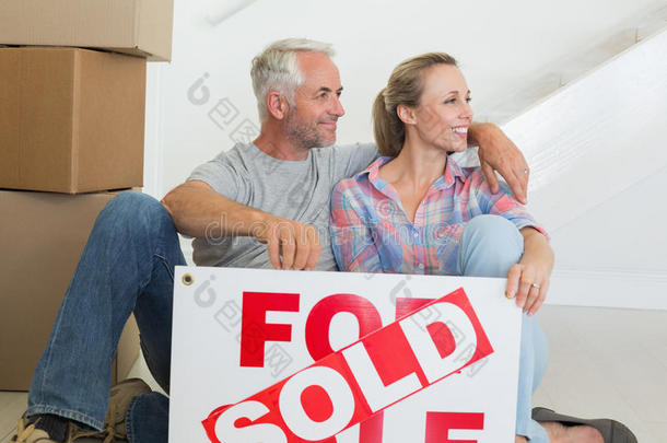 一对幸福的夫妇坐在地板上挂着卖的牌子