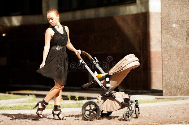时髦的现代妈妈坐着婴儿车在城市街道上。年轻的母亲