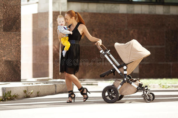时髦的现代妈妈坐着婴儿车在城市街道上。年轻的母亲