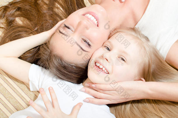 美丽迷人的母亲或姐妹与小女孩面对面躺着开心地微笑着看着相机