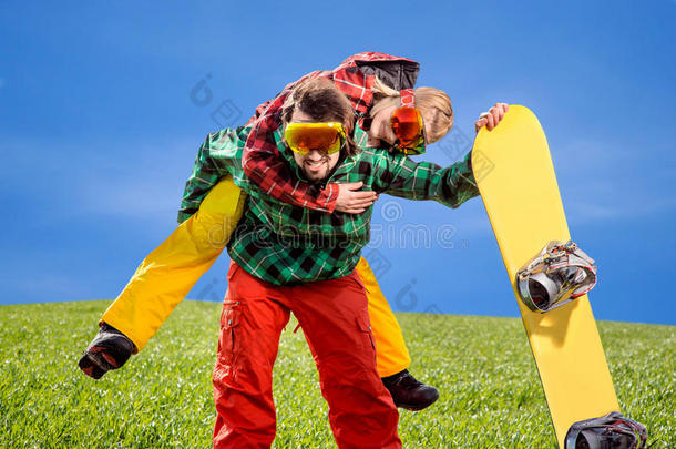 身穿滑雪服的男子背着滑雪板在天底下的草地上给女友搭车