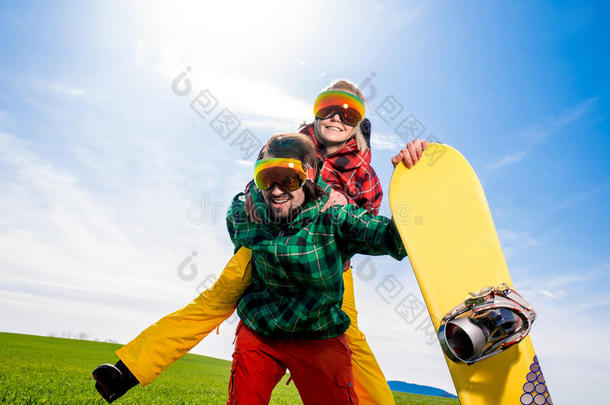 身穿滑雪服的男子背着滑雪板在天<strong>底下</strong>的草地上给女友搭车