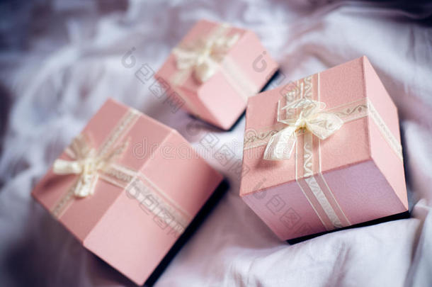 3个华丽漂亮的豪华盒子粉色礼物，白色床上有白色丝带背景图片
