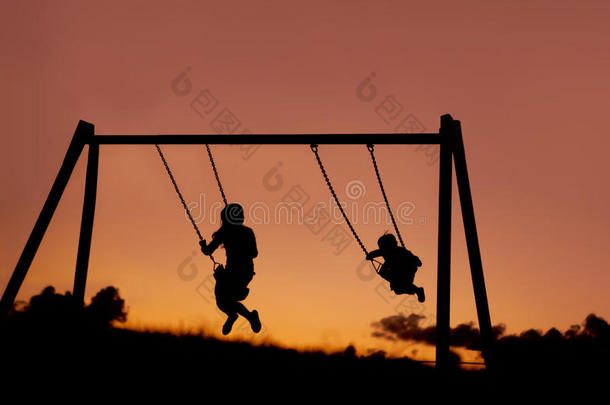 两个孩子在夕阳下荡秋千的剪影。