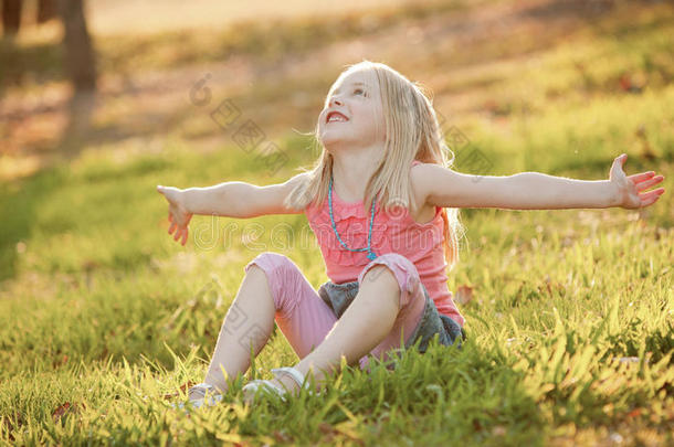 夏天，一个金发碧眼的小女孩坐在草地上的背光下。她伸出双臂代表自由，<strong>投降</strong>或是ha