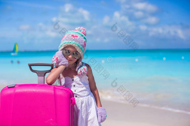 一个可爱的小女孩，戴着温暖的冬天的帽子和手套在热带海滩上