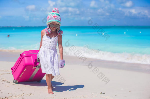 可爱的女孩戴着温暖的冬日帽，戴着手套，提着行李在沙滩上散步