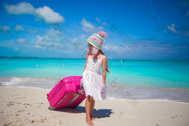 可爱的女孩戴着温<strong>暖</strong>的<strong>冬日</strong>帽，戴着手套，提着行李在沙滩上散步
