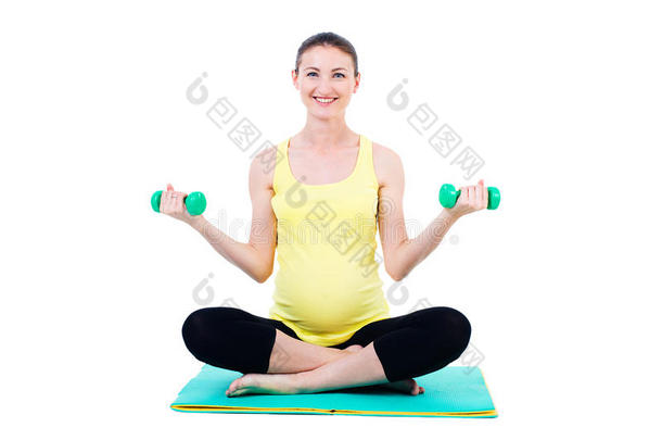 笑眯眯的孕妇举着哑铃坐在垫子上