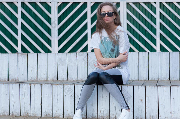 那个戴着墨镜长发的漂亮女孩坐在白色的<strong>木台阶</strong>上。