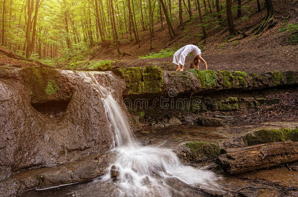 女人在自然瀑布练习瑜伽。森林；乌尔德瓦-法努拉萨纳；达努拉萨纳姿势