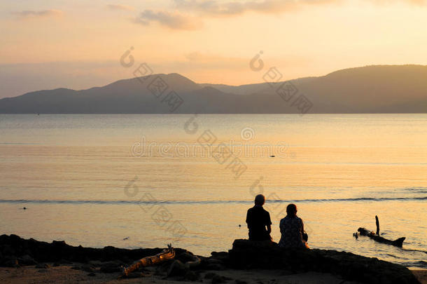 西尔霍特夫妇坐在海滩黄昏日落山脉背景