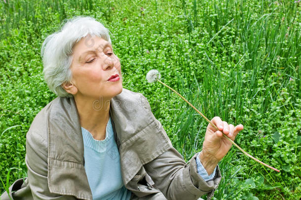 快乐的老妇人坐在草地上吹蒲公英