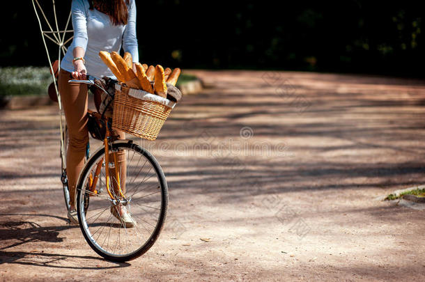 一个女人骑着自行车，<strong>篮子里</strong>装满了法式面包