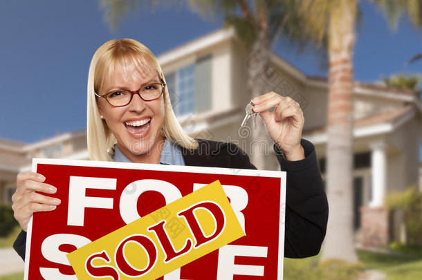 兴奋的女人拿着房子的钥匙和卖房产的牌子
