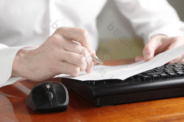手拿着文件和笔在电脑键盘上