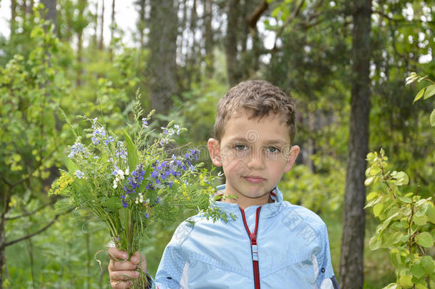 拿着一束花站在树林里的男孩。