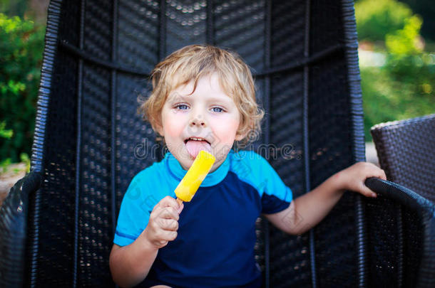 可爱的金发男孩在户外吃黄色的冰激凌