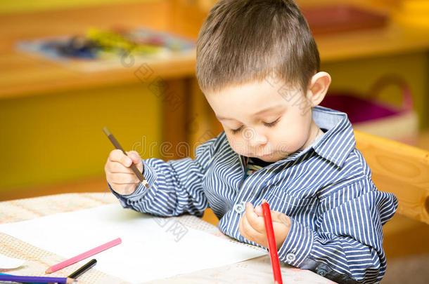 幼儿园小男孩在幼儿园桌边用彩色<strong>铅笔画画</strong>