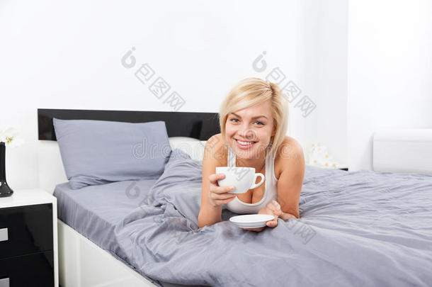 女人端着一杯咖啡躺在床上