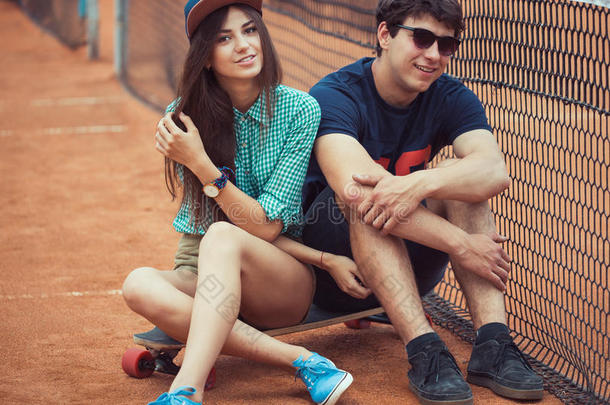 一对年轻夫妇坐在网球场上的滑板上