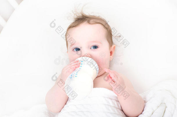 可爱的婴儿在白色婴儿床上从瓶子里<strong>喝牛奶</strong>
