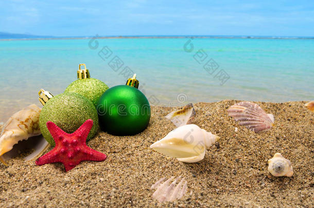 圣诞球和贝壳在沙子上与夏天的海洋