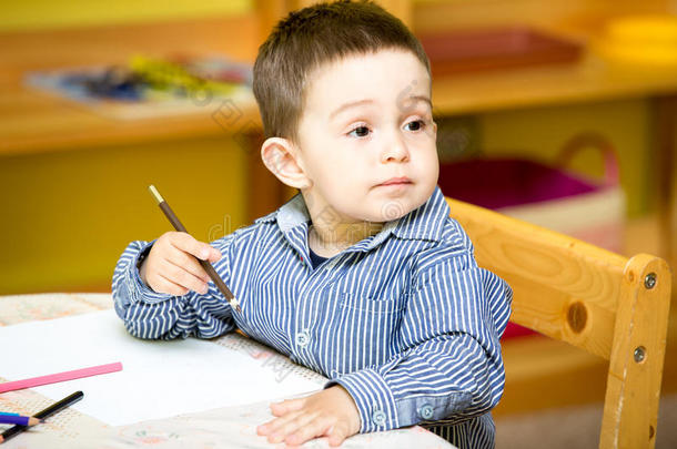 幼儿园小男孩在幼儿园桌边用彩色铅笔画画