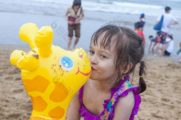 在海滩上玩耍的小女孩亲吻玩具长颈鹿