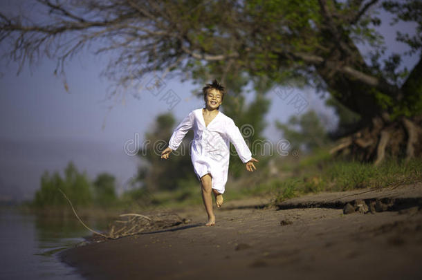 快乐的男孩穿着白衬衫，沿着河岸奔跑