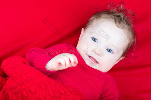 可爱的婴儿穿着红色毛衣在红色毯子下