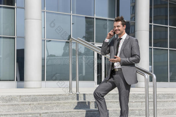 面带微笑的商人站在办公室外的台阶上用手机打电话
