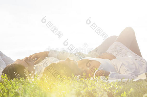 一对年轻夫妇躺在草地上，天空<strong>晴朗</strong>